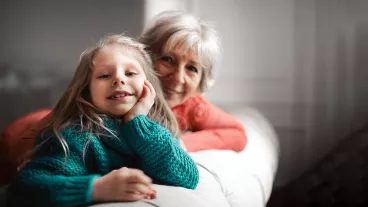 A girl and her grandma sitting on a sofa and smiling at the camera