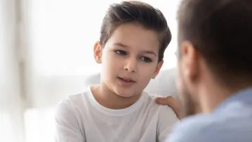 Back view of dad sit on couch with son talking sharing thoughts or problems,  support him showing care and understanding