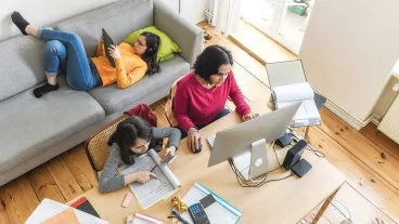 Young mother working on her computer with her daughters playing on their mobile devices