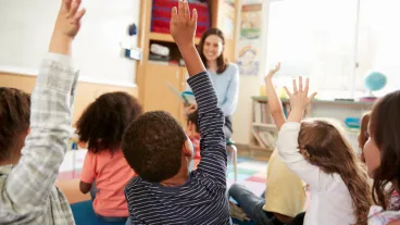 Elementary school kids raising hands to teacher, back view