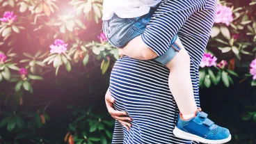 Pregnant woman with child. Mother and son on nature background, close-up. Child boy is sitting on belly of his mother, who pregnant for second time. Pregnancy, new life, family, parenthood concept.