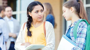 Serious teenage girls discuss an upcoming exam as they wait for school to start