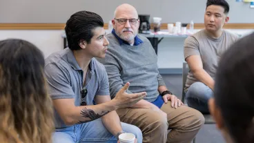 Mid adult male army veteran has an intense conversation with an unrecognizable person during a support group meeting. He gestures while speaking.
