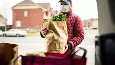 Mature man wearing protection mask, unloading grocery from car trunk