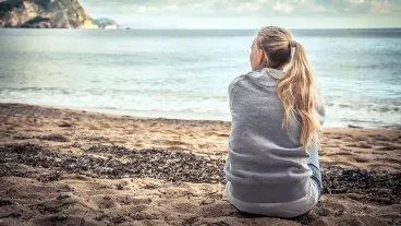 teenage girl sitting on beach looking out at the sea