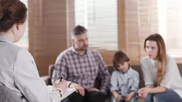 Rear view of female psychologist helping young family with a child to solve family problems. Family sitting on a sofa in the blurred background