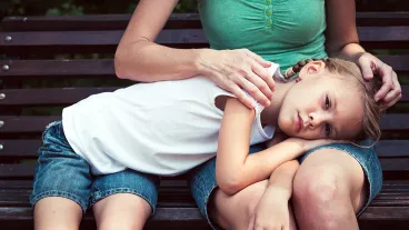 Sad mother and daughter sitting on bench in the park at the day time.