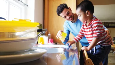 A young father doing dishes with his son