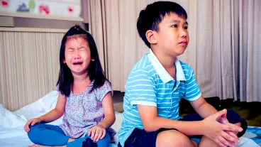 A photo of two children sitting on the floor. The boy who is older is sitting with his back to the younger girl and she is crying.