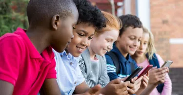 Group of multiethnic children sitting in a row and typing messages on their smartphones.