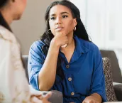 An empathetic mid adult female counselor sits with her hand on her chin as she listens to the unrecognizable mid adult female client.