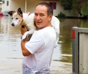 Man holding a dog on his shoulders as he stands in waist deep flood waters. 