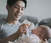 Young father feeding his baby boy son with milk bottle at living room during weekend