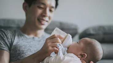 Young father feeding his baby boy son with milk bottle at living room during weekend